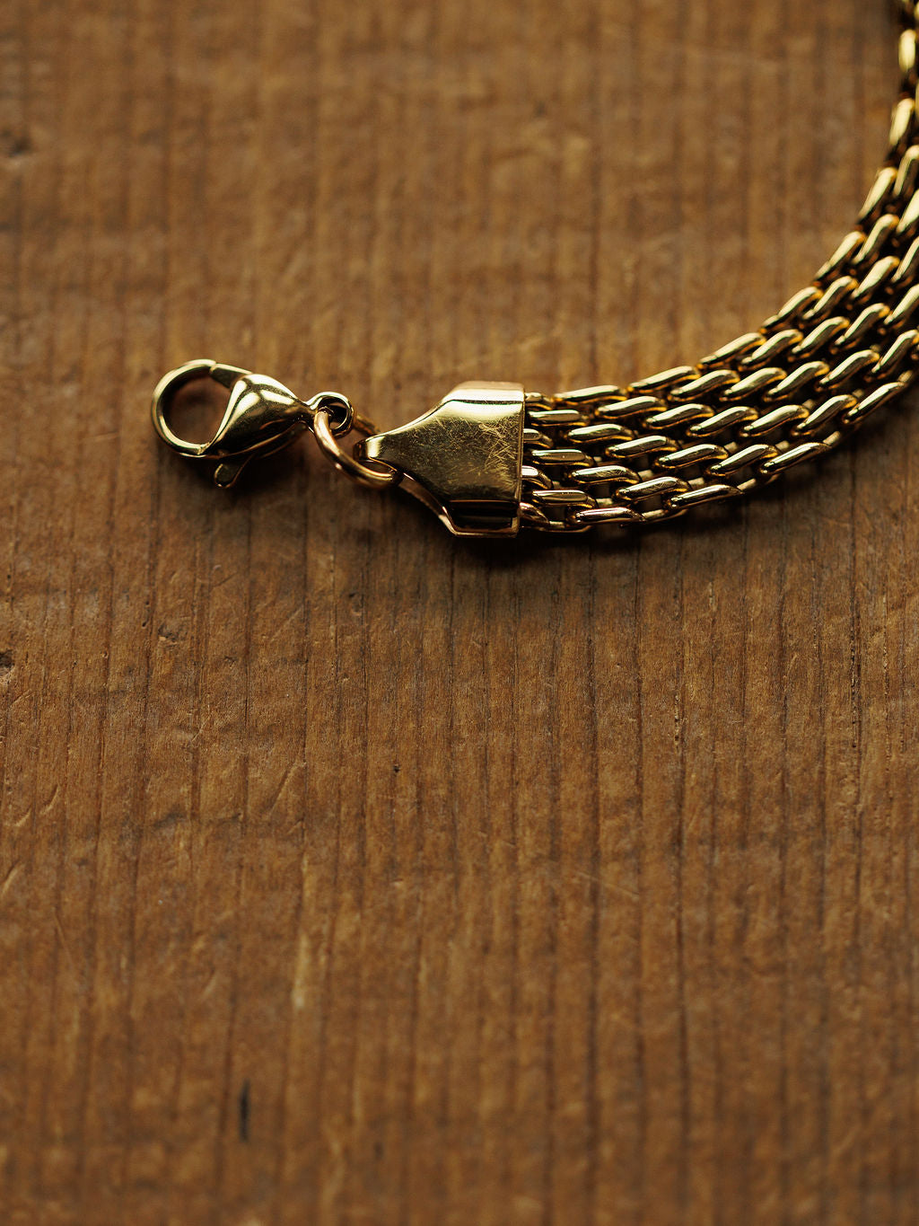 A close-up of the Vienna Bracelet by Savannah Sevens western life{&}style, an 18K gold filled, hypoallergenic braided chain with a lobster clasp, displayed on wood with visible grain and texture.