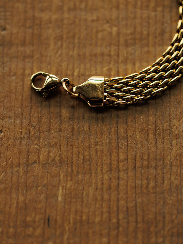 A close-up of the Vienna Bracelet by Savannah Sevens western life{&}style, an 18K gold filled, hypoallergenic braided chain with a lobster clasp, displayed on wood with visible grain and texture.