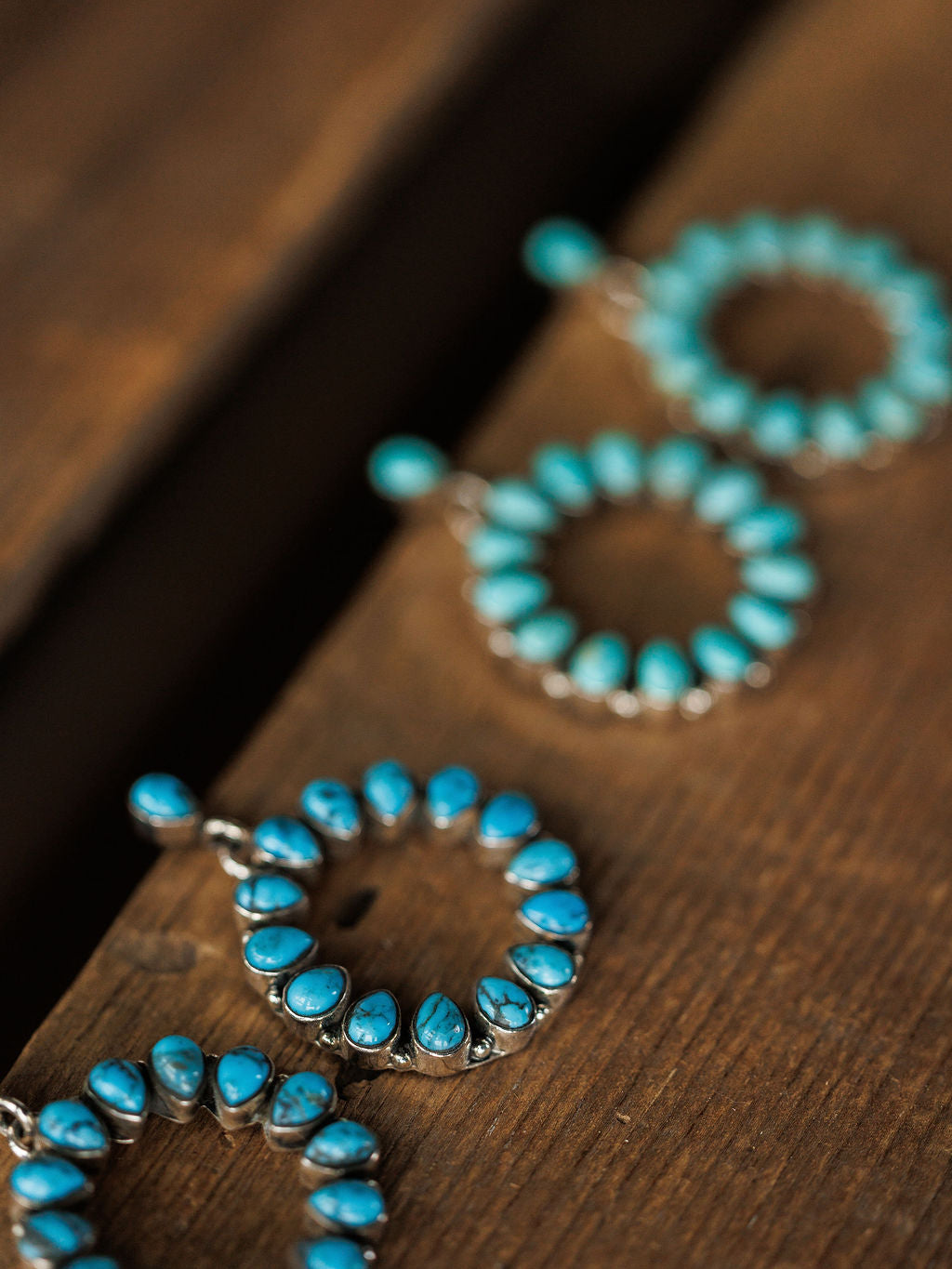 Close-up of two pairs of Savannah Sevens western life{&}style Ocala Earrings, crafted from sterling silver with Kingman turquoise stones in a circular design, displayed on a wooden surface.
