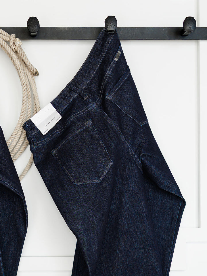 The Brody High Rise Wide Leg Jean by Savannah Sevens western life{&}style hangs on a black wall hook rack next to a coiled rope against a white wall.