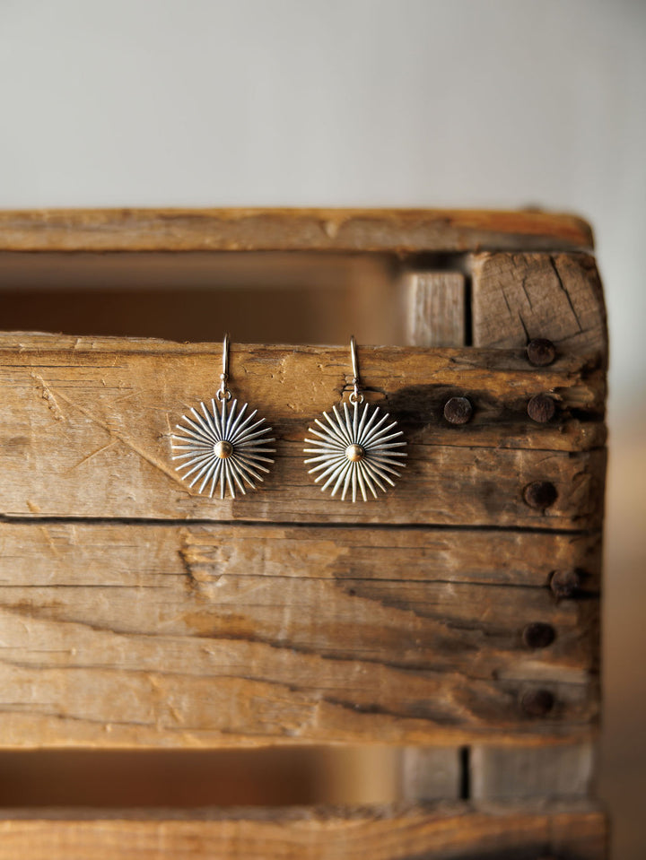 A pair of Rowel Earrings {Small} by Savannah Sevens western life{&}style, handcrafted with radiating spokes and a central bead, hang side by side on a rustic wooden box with a softly blurred background.