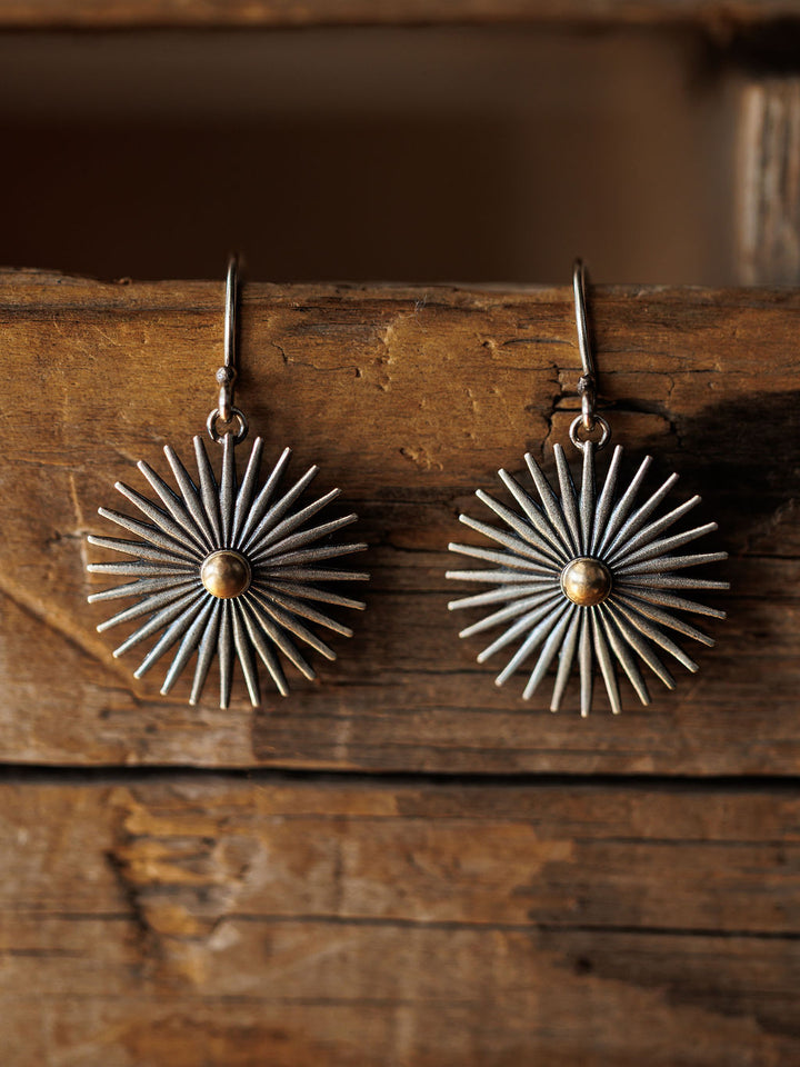 A pair of Rowel Earrings {Small} by Savannah Sevens western life{&}style, featuring sterling silver with gold-toned centers, hang on a rustic wooden surface.