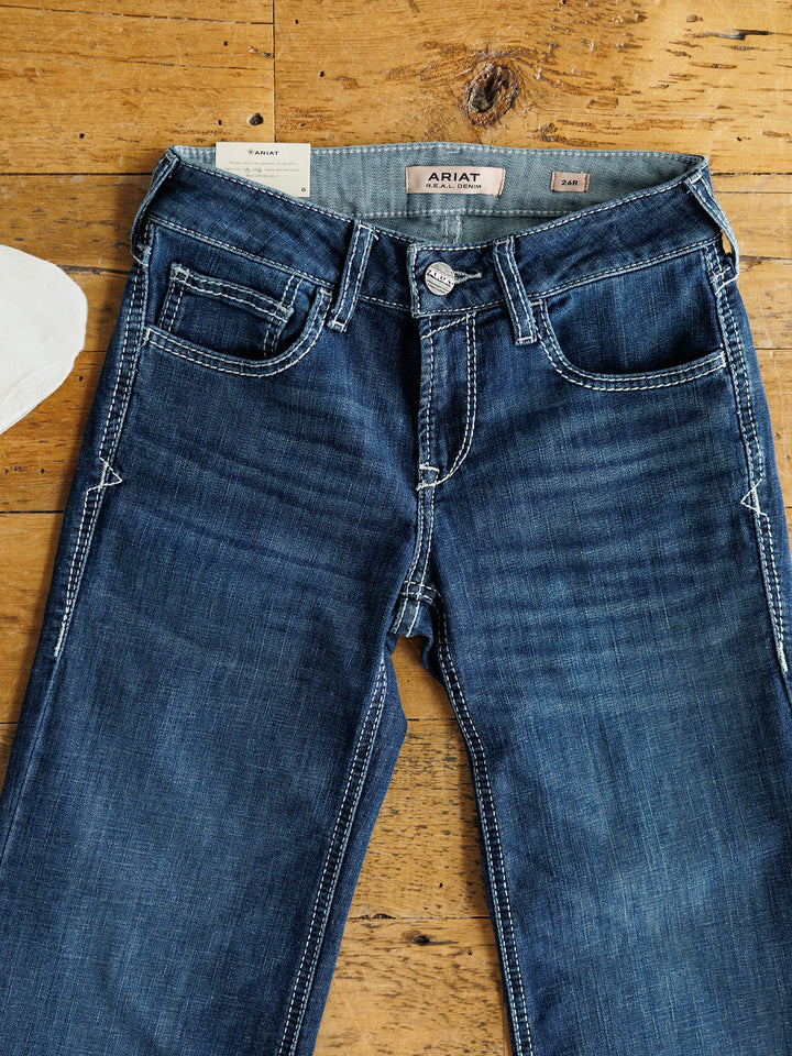 The Tripp Perfect Rise Trouser Jean by Savannah Sevens western life{&}style is shown in a medium dark wash with white stitching, front pockets, belt loops, and a comfortable no-gap waist laid flat on a wooden surface.