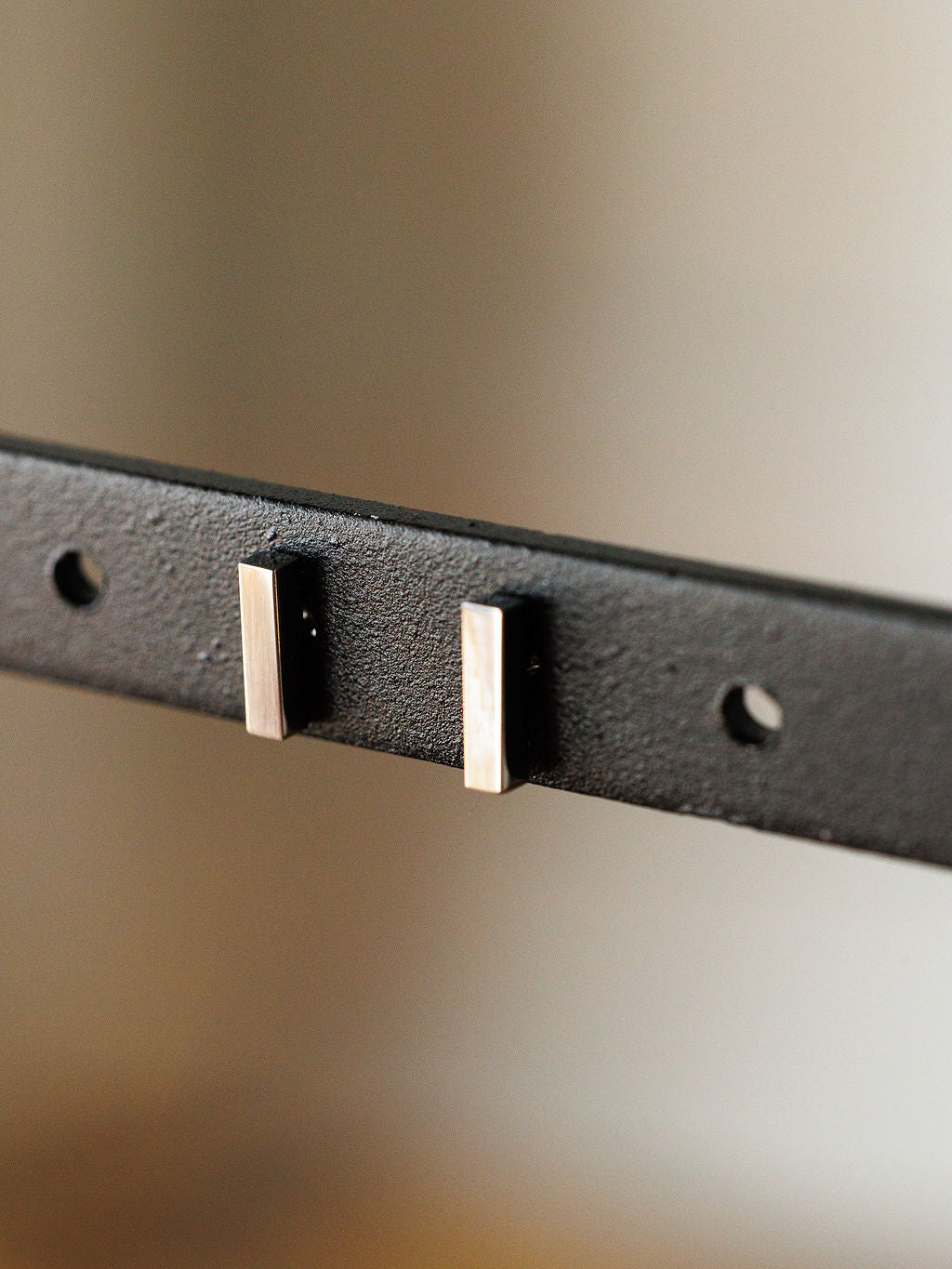 Close-up of the Lexington Earrings by Savannah Sevens western life{&}style—black metal bar studs featuring two rectangular silver pegs and three round holes, set against a blurred neutral background.