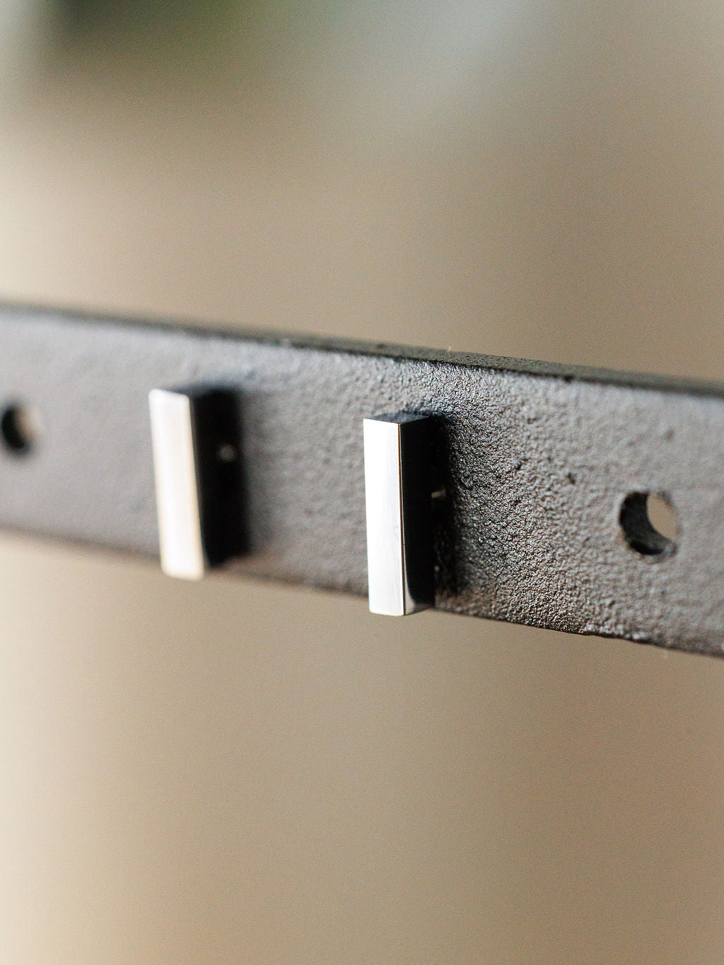 Close-up of the Lexington Earrings by Savannah Sevens western life{&}style—two rectangular silver bar studs on a black metal bracket with two empty circular holes, viewed at an angle against a blurred background.