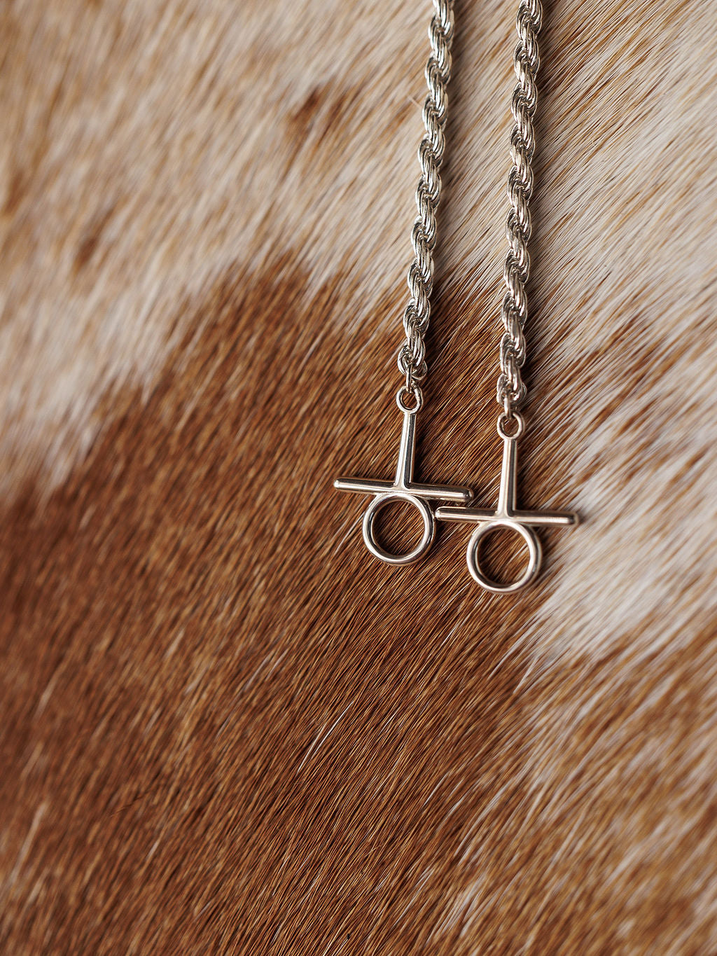 The Wild At Heart Bolo necklaces by Savannah Sevens western life{&}style, featuring silver chains and toggle clasps inspired by Western jewelry, are displayed on a brown and white cowhide background.