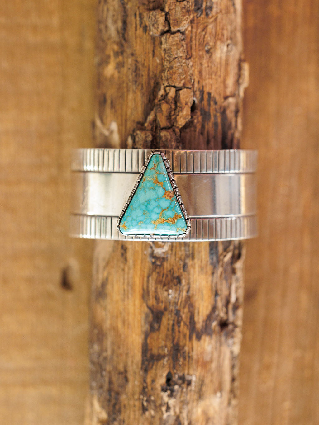 The Vallejo Cuff by Savannah Sevens western life{&}style features a triangular turquoise stone set in a sterling silver cuff with textured edges and a smooth center, displayed vertically against rustic wood.