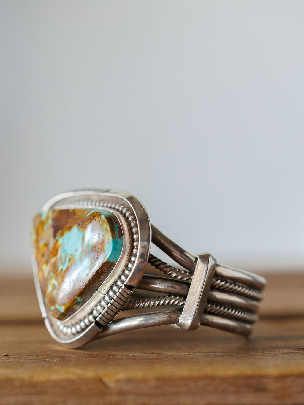 A close-up of the Sedalia Cuff by Savannah Sevens western life{&}style, a sterling silver bracelet featuring a large polished stone with brown, tan, and turquoise patterns inspired by Native American jewelry, resting on wood.