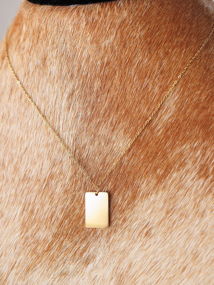 A close-up of the Avera Necklace by Savannah Sevens western life{&}style, an 18K gold coated, tarnish resistant square pendant, worn around the neck of a light brown cowhide with white spots.