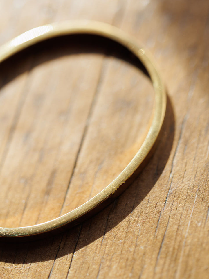 A close-up of the Sallis Bracelet by Savannah Sevens western life{&}style rests on wood, sunlight casting soft shadows that highlight the gold metal’s texture and the grain of the surface.