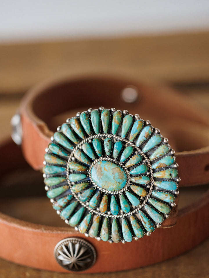 A close-up of the Savannah Sevens western life{&}style Holyoke Buckle: a brown leather belt with an ornate oval sterling silver buckle, Kingman turquoise stones, and radiating silver accents.