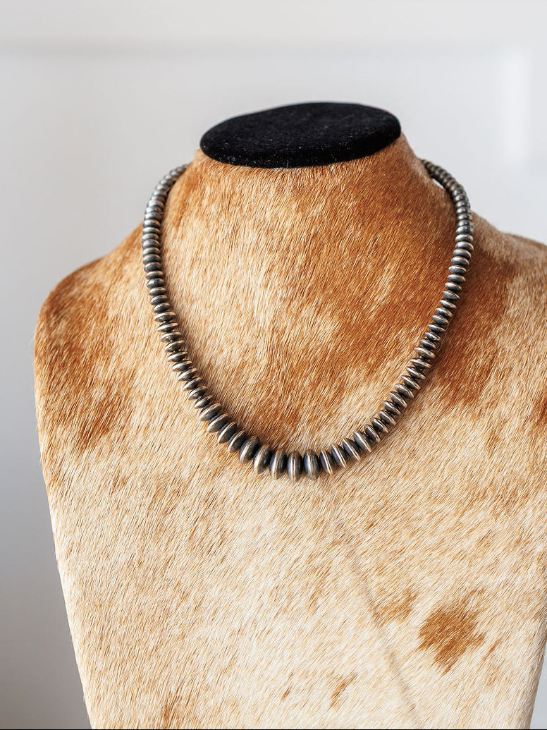 The Saledo Necklace by Savannah Sevens western life{&}style, a 20.5-inch sterling silver Navajo pearl necklace with graduated rondelle beads, is shown on a tan and white cowhide jewelry bust against a light background.