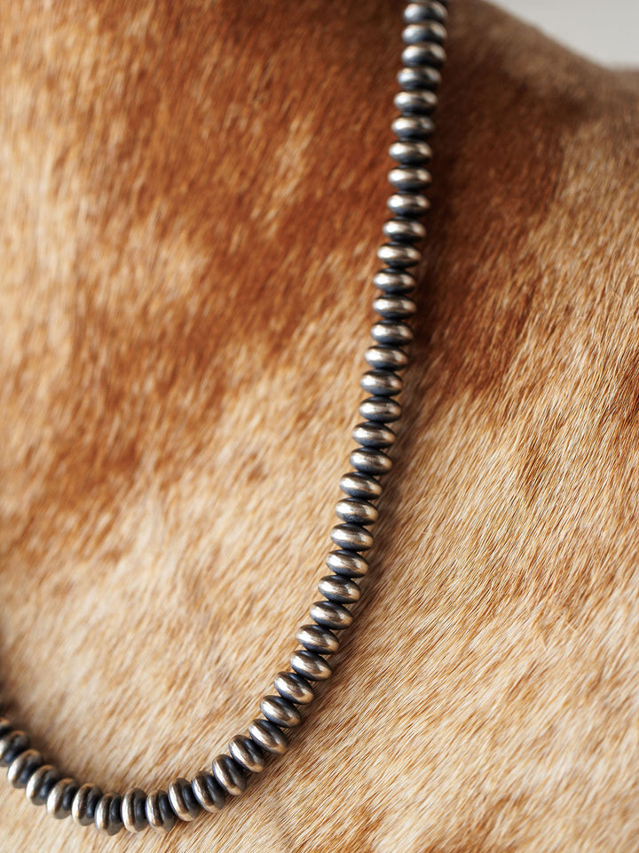 A close-up of the Tecopa Necklace by Savannah Sevens western life{&}style, a sterling silver Navajo pearl design, shown resting on a person's neck and upper chest with light brown and cream cowhide in the background.