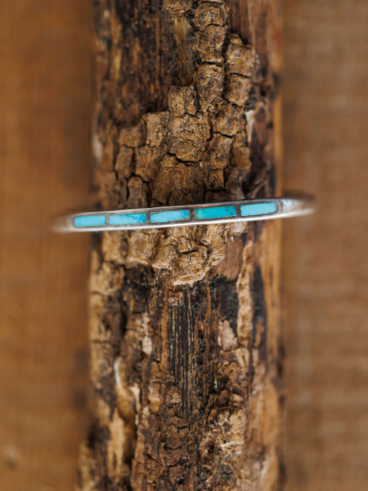 The Ponderosa Cuff by Savannah Sevens western life{&}style, a silver bracelet featuring five rectangular turquoise inlays, is displayed vertically on textured wood with a brown background.