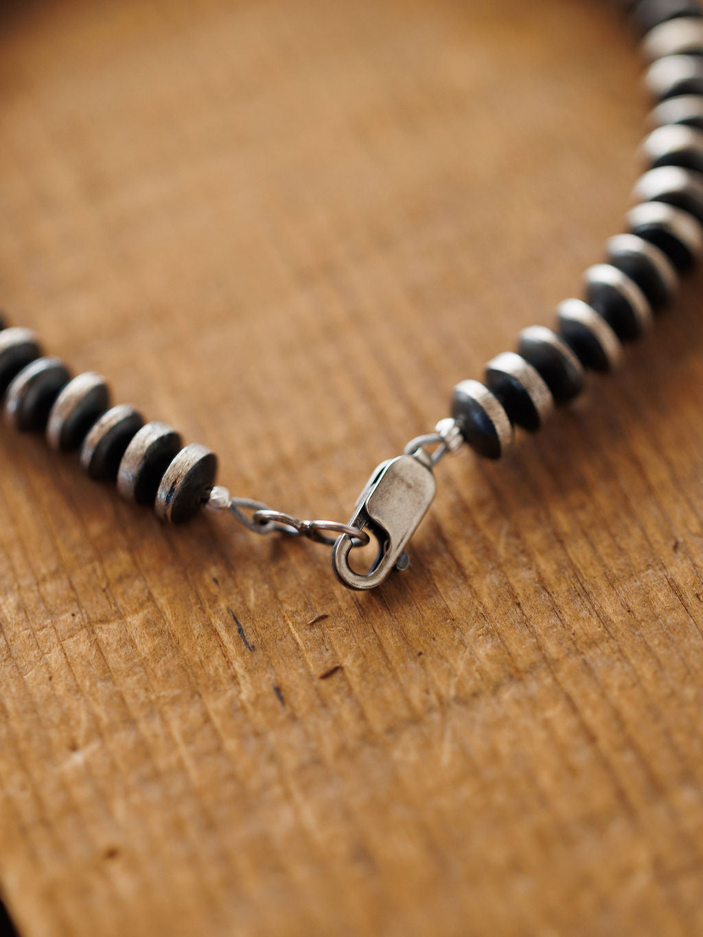 Close-up of the Rowlett Bracelet by Savannah Sevens western life{&}style, with alternating black and sterling silver 4mm rondelle beads and a silver clasp, displayed on textured wood.