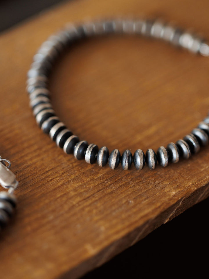 A close-up of the Rowlett Bracelet by Savannah Sevens western life{&}style shows alternating black and sterling silver 4mm rondelle beads resting on wood, evenly spaced and forming a partial circle.