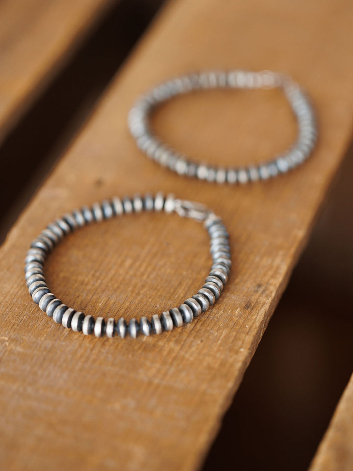 Two Rowlett Bracelets by Savannah Sevens western life{&}style, made with 4mm sterling silver rondelle beads in a Navajo pearl style, are displayed on wood—one sharply in focus in front, the other blurred in the background.