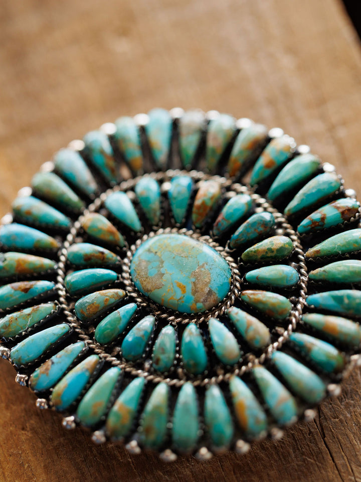 A close-up of the Holyoke Buckle by Savannah Sevens western life{&}style, featuring concentric rows of oval Kingman turquoise set in sterling silver, displayed on a wooden surface.