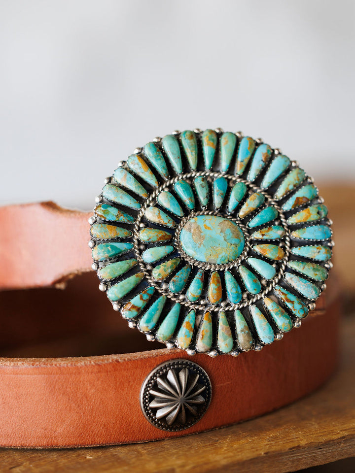 A close-up of the Holyoke Buckle by Savannah Sevens western life{&}style— a tan leather belt with a large round sterling silver and Kingman turquoise buckle with radiating turquoise stones, plus a smaller silver concho on the leather.
