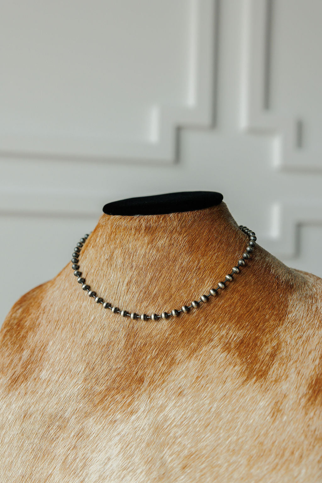 The Sedalia Necklace by Savannah Sevens western life{&}style is showcased on a brown and white cowhide mannequin against a white textured background.