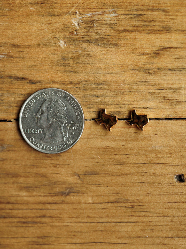 A U.S. quarter and the Texas Earrings by Savannah Sevens western life{&}style are displayed on a wooden surface.