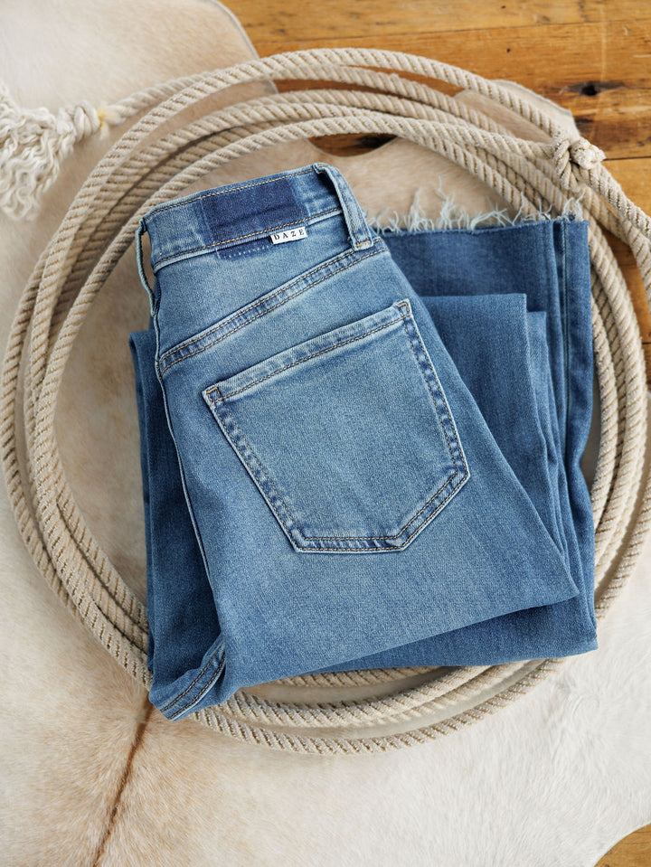 A pair of Savannah Sevens western life{&}style The Jacey High Rise Wide Leg Jeans is neatly folded inside a coiled rope, resting on a light cowhide rug atop a wooden floor.