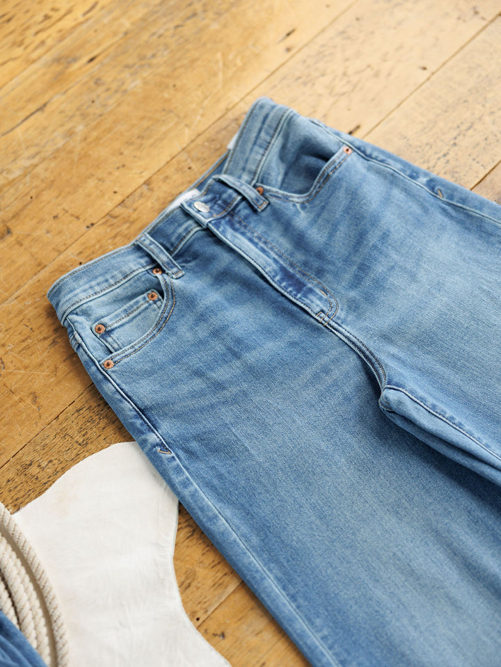 A pair of The Jacey High Rise Wide Leg Jeans by Savannah Sevens western life{&}style in light blue lies flat on a wooden floor beside a white faux fur rug and a coiled rope.