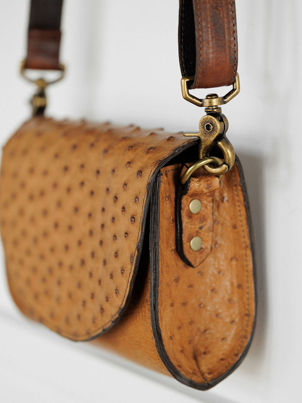 Close-up of The Chicota by Savannah Sevens western life{&}style, featuring textured brown ostrich-pattern leather, a brass buckle with rivets, and a dark brown leather strap.