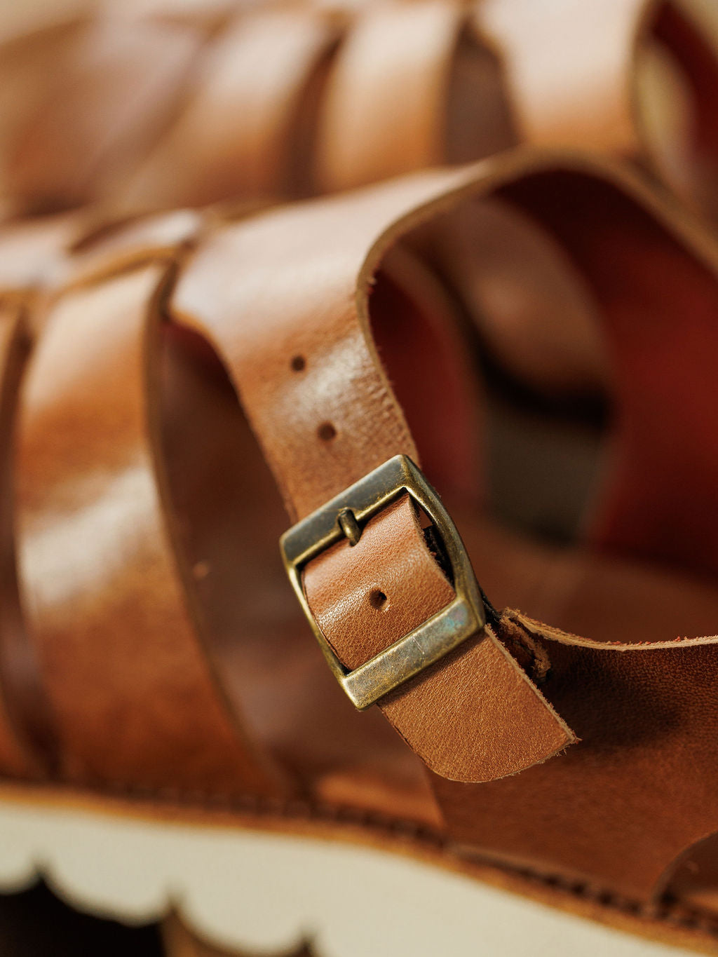 Close-up of The Tuscola by Savannah Sevens western life{&}style: leather platform sandal with a brass buckle, textured leather straps, precise stitching, white scalloped sole, and cushioned insole for comfort.