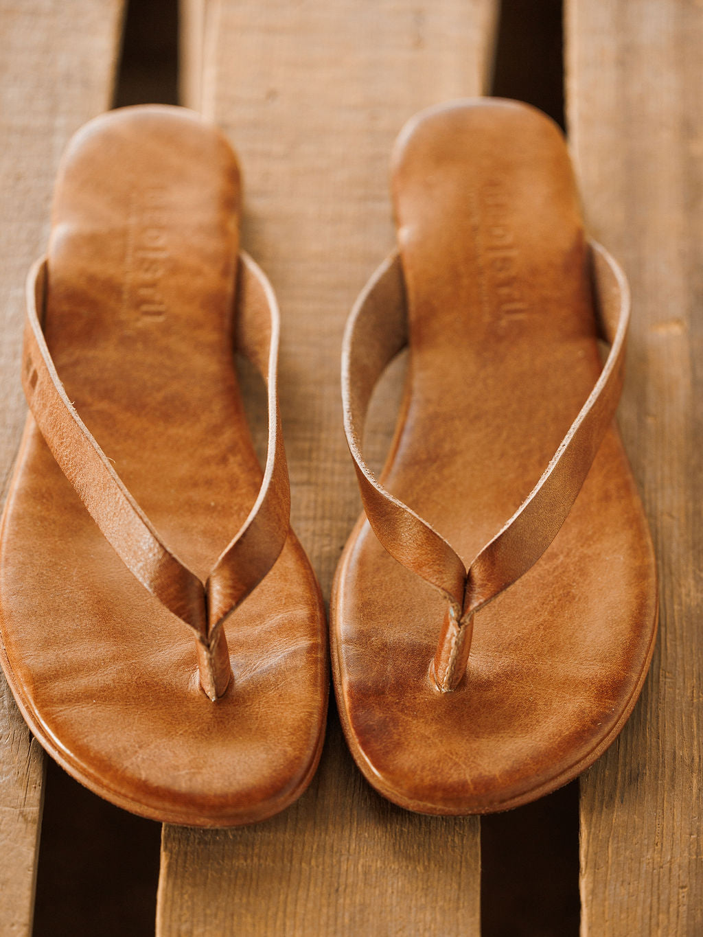 A pair of The Sadler leather flip-flop sandals by Savannah Sevens western life{&}style with cushioned footbeds, placed side by side on a wooden surface.