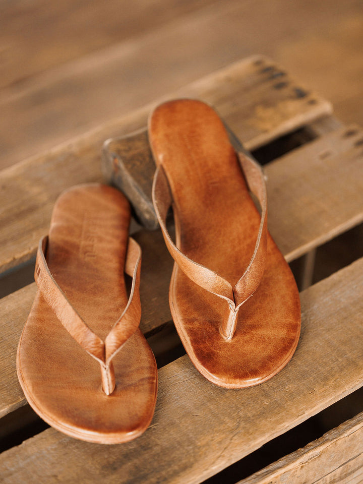 The Sadler leather flip flop sandals by Savannah Sevens western life{&}style, featuring a cushioned footbed, are displayed on a rustic wooden surface. Sandals made by BedStu. 