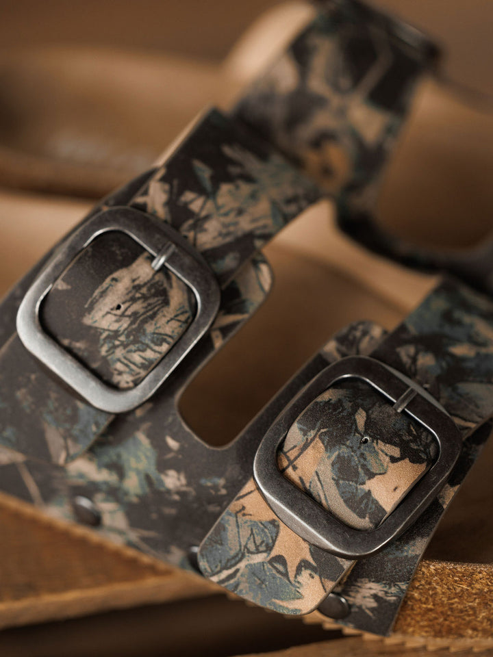 Close-up of The Kane by Savannah Sevens western life{&}style, a camo slip-on sandal with two metal buckles, camouflage-patterned straps, and a cork footbed featuring arch support for comfort.