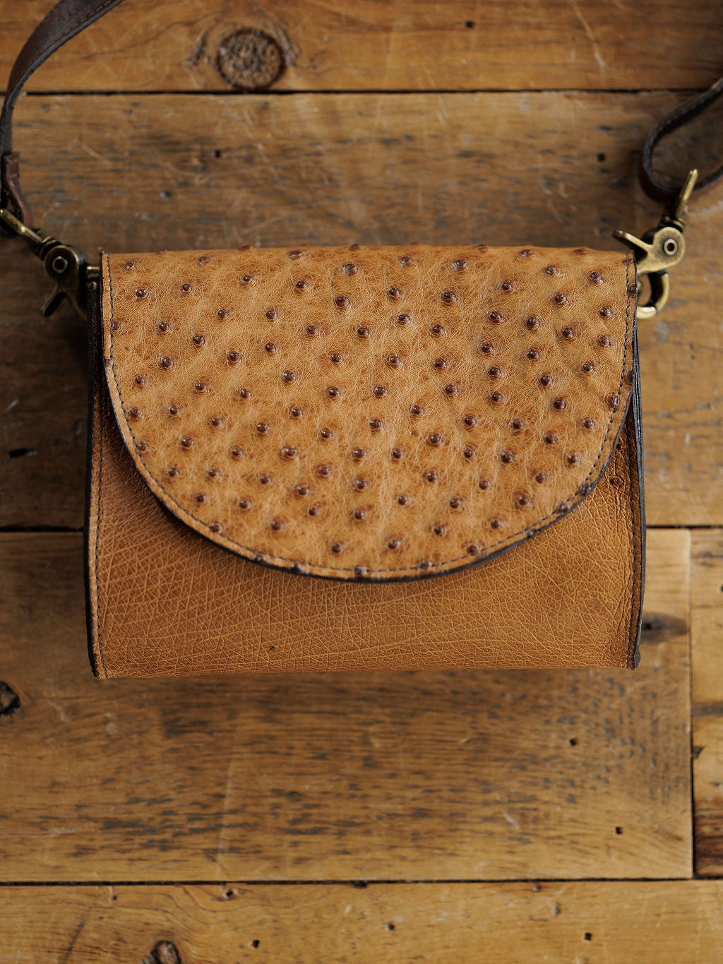 The Chicota by Savannah Sevens western life{&}style is a small saddle tan women’s crossbody with a textured, ostrich-style dotted flap, shown on a rustic wooden surface.