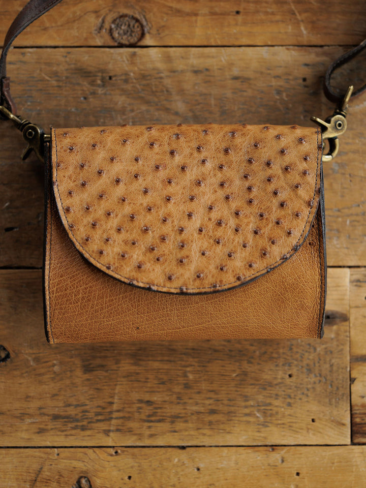 The Chicota by Savannah Sevens western life{&}style is a small saddle tan women’s crossbody with a textured, ostrich-style dotted flap, shown on a rustic wooden surface.