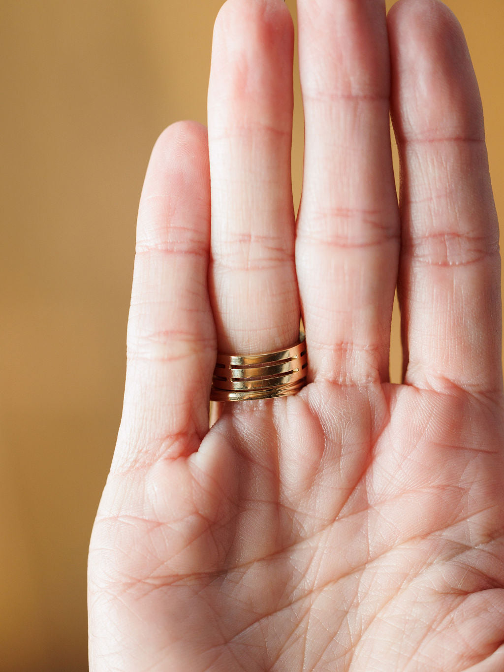 A close-up of an open hand facing the camera, wearing the Savannah Sevens western life{&}style Diamond Turquoise Ring with horizontal grooves on the ring finger, set against a softly blurred warm background. Collaboration the Devereaux Gold.