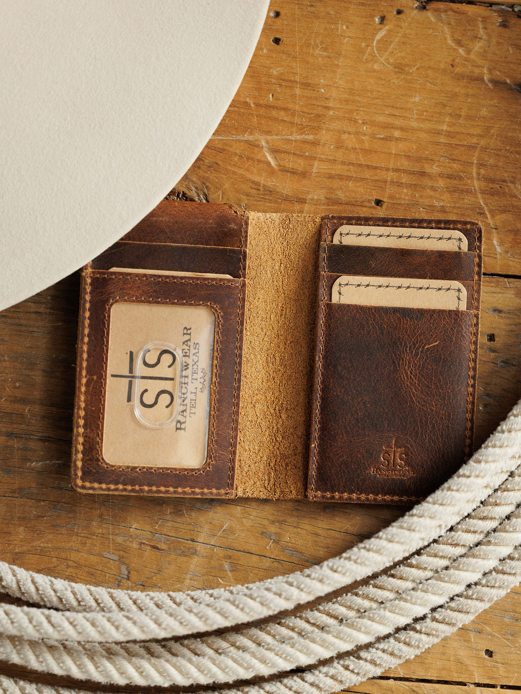 The Waynesboro Money Clip Wallet by Savannah Sevens western life{&}style sits open on a rustic wooden surface, revealing card slots and an ID window.