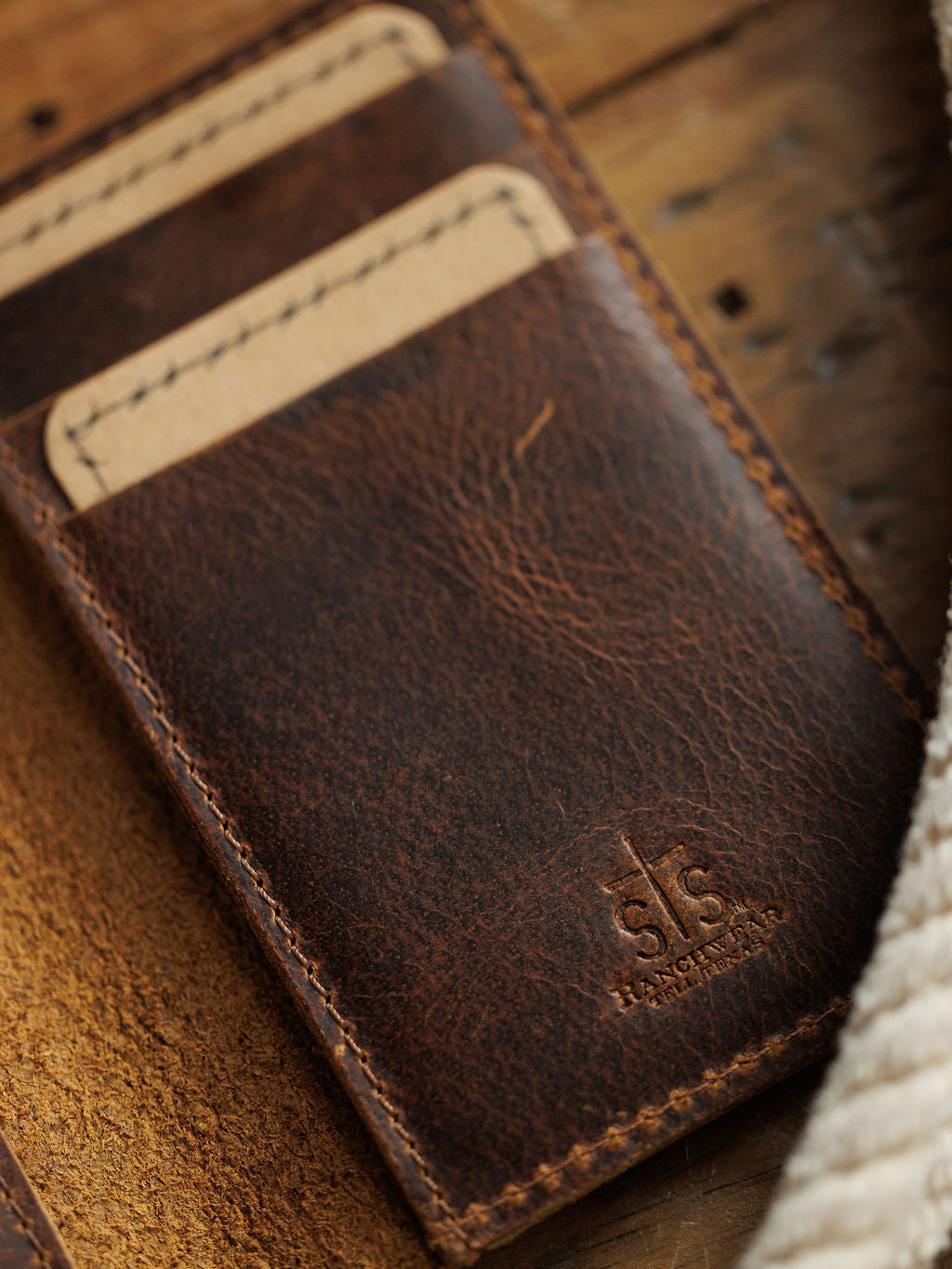A close-up of the Waynesboro Money Clip Wallet by Savannah Sevens western life{&}style, crafted from full grain leather with two card slots holding tan cards, and embossed branding near the bottom edge on a wooden surface.