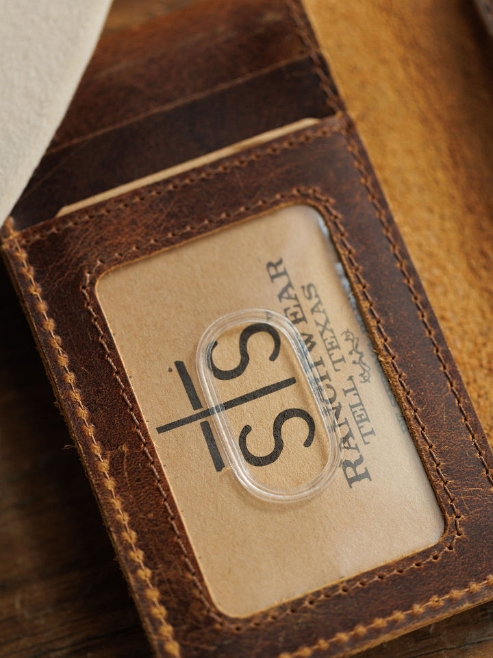 A close-up of the Waynesboro Money Clip Wallet by Savannah Sevens western life{&}style, showing a business card with STS and Ringwear, Texas visible through its transparent window slot.