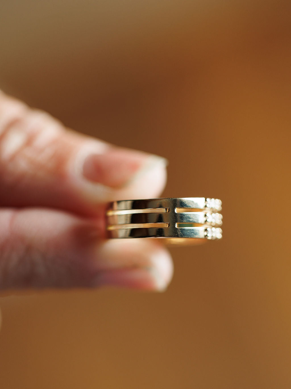 A close-up of a hand holding the Savannah Sevens western life{&}style Diamond Turquoise Ring with three parallel grooves and Southwest turquoise accents, set against a blurred warm brown background.