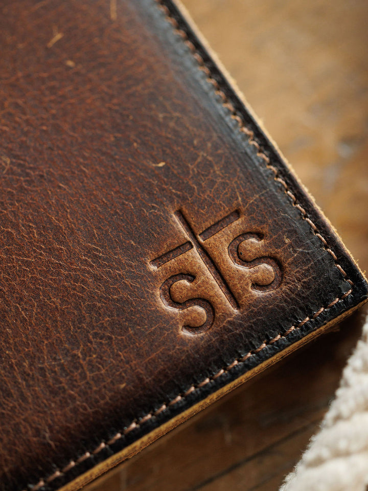 Close-up of the Waynesboro Hidden Cash Wallet by Savannah Sevens western life{&}style, showcasing distressed full grain leather, visible stitching, and an embossed cross logo with “sts,” highlighting the texture and craftsmanship.