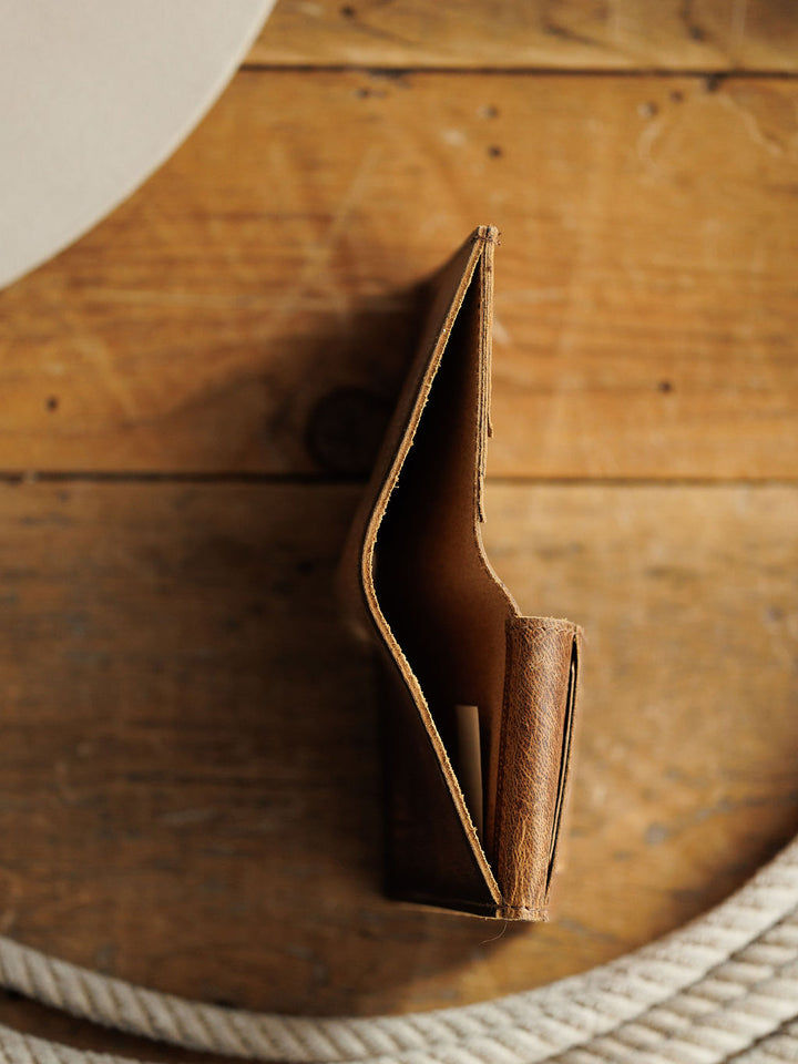 A top-down view of the Savannah Sevens western life{&}style Waynesboro Hidden Cash Wallet in distressed full grain leather rests on a wooden surface, with a white rope partly visible at the bottom edge.