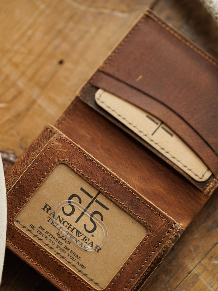 The Waynesboro Hidden Cash Wallet by Savannah Sevens western life{&}style is a brown distressed full grain leather men’s wallet with visible stitching, clear ID slot, and card slot, shown resting on a wooden surface.