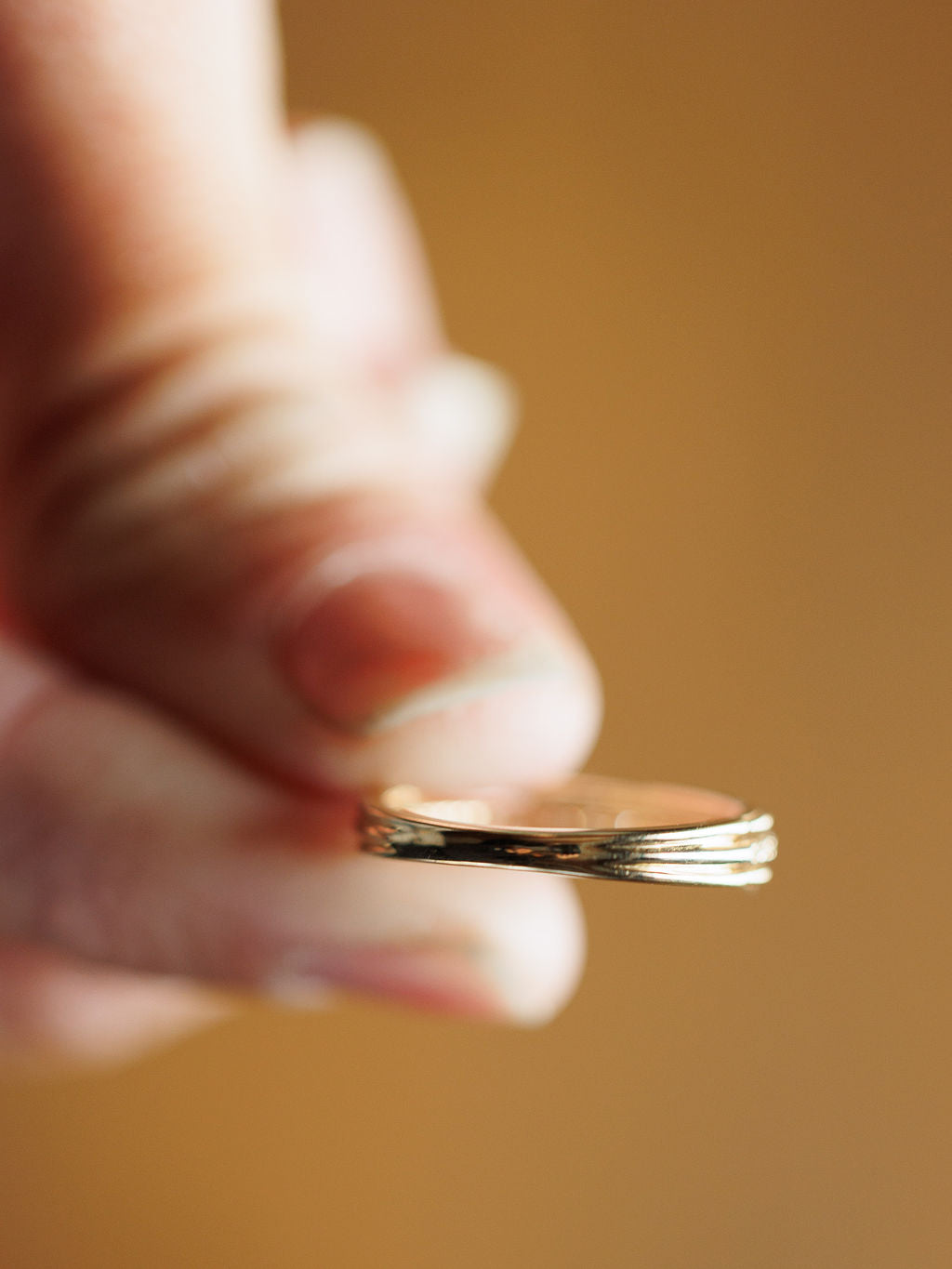 A hand holds three gold coins between thumb and finger against a blurred brown background, echoing the intricate detail of the Diamond Milgrain Ring by Savannah Sevens western life{&}style.