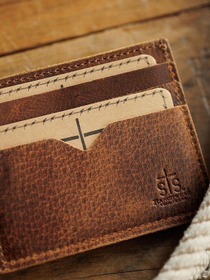 Close-up of the Waynesboro Bifold Wallet by Savannah Sevens western life{&}style, crafted from distressed full grain leather with visible stitching. The wallet sits on wood, showcasing its embossed logo.