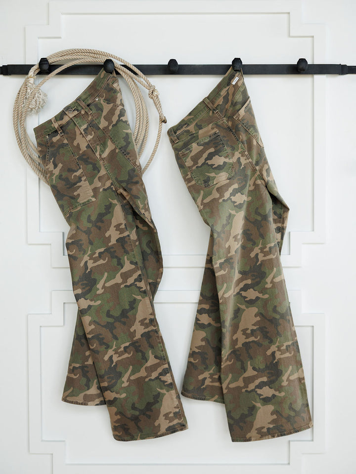 Two pairs of The Granger High Rise Wide Leg Jeans by Savannah Sevens western life{&}style in a camo print hang on black hooks against a white wall, with a coiled rope on the hook to the left of the jeans.