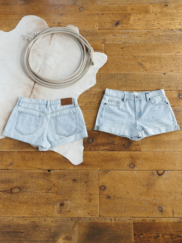 Two pairs of The Mackie Shorts by Savannah Sevens western life{&}style are laid flat on a wooden floor—one showing the front, one the back. A looped rope sits on a white animal hide rug in the upper left corner.