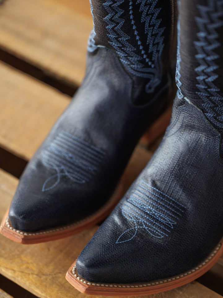 Close-up of The Pasadena boots by Savannah Sevens western life{&}style in midnight navy leather with blue stitching and a western snip toe, displayed on a wooden surface.