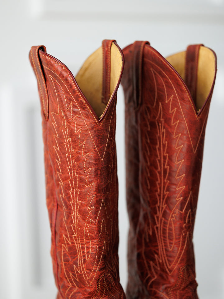 A close-up of two "The Pueblo" boots by Savannah Sevens western life{&}style, made from distressed leather with detailed stitching, standing side by side against a softly blurred background.