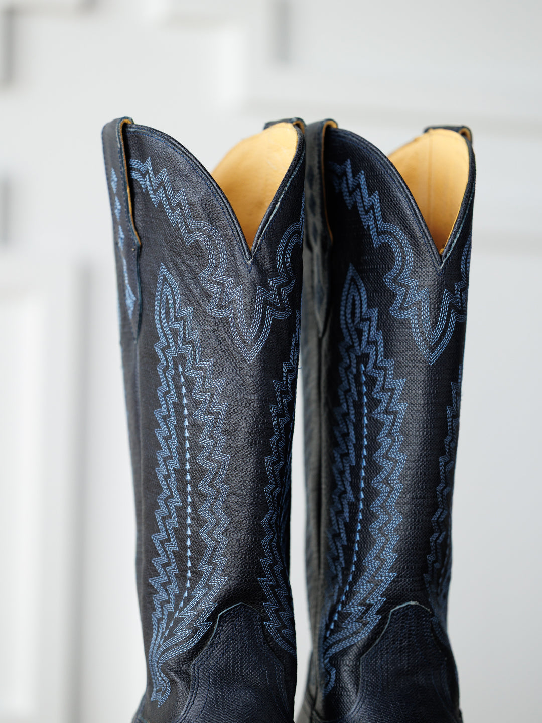 Close-up of The Pasadena boots by Savannah Sevens western life{&}style, featuring blue stitching and elegant midnight navy leather accents on the upper, set against a softly blurred background.