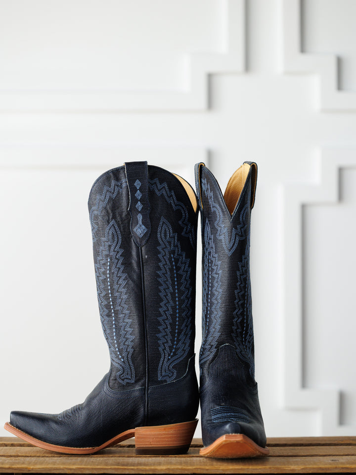 A pair of The Pasadena boots by Savannah Sevens western life{&}style, featuring decorative stitching and brown wooden heels—one upright, one leaning—displayed on wood with a white geometric-patterned background. Boots made by Black Star. 
